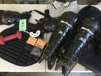 Full view of MacGregor umpire gear set laid out on table including chest protector, leg guards, arm guards, throat guards, umpire shirt, and red dumbbell.