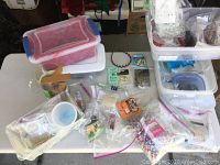 Overview of arts and crafts lot with plastic containers, bags of beads and feathers, and various craft materials spread on a table.