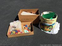 Overall lot view showing three main containers: vintage Lincoln Logs box filled with logs, a cardboard box with wooden blocks and checkers, and a plastic bag of shape blocks