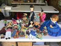 Photo of diverse collection of approximately 21 dolls laid out on table