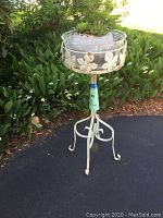 Full view of white metal plant stand holding the artificial succulent arrangement outdoors against greenery.