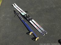Full view of two Fischer Vista Crown cross country skis, two blue Swix ski poles, and one pair of women's Rossignol ski boots size 8.5 on pavement.