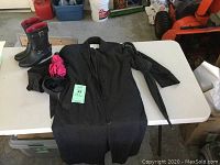 Full lot overview showing black trench coat, pair of black booties with buckle, folded umbrellas on table.