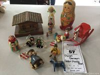 Photo of all lot items displayed on a tabletop including wooden chalet music box, several nesting dolls, small folk figurines, and a red wooden sleigh.