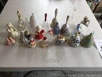 Overview of 20 collectible bells on table showing variety of materials and designs.