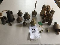 Photo of varied metal animal bells, including rusted iron bells with twine, brass/bronze engraved bells, and small hanging bells.