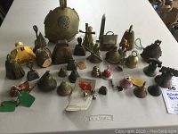 Full spread of multiple bells on a white table showing varied sizes and tagged provenance.