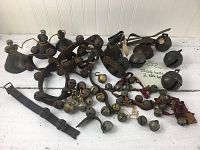 Wide shot showing full group of antique and vintage sleigh bells and Mexican pottery bells arranged on a white surface.