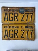 Pair of 1956 California license plates AGR 277 laid flat showing front and back plates, some rust and wear visible