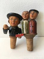 Front view of two hand-carved wooden bottle corks with moving features.