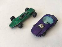 Two Hot Wheels toy cars displayed; one green Formula 1 style, one purple futuristic style with canopy and engine detail, both showing wear.