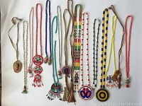 Full view of all 16 vintage First Nations beaded necklaces arranged on white background, showing variety of pendants, bead colors, and styles.