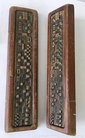 Front view of two rectangular wood framed door handles with dark metal insets featuring geometric designs with various shapes and patterns.