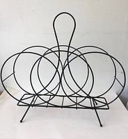 Front view of a black metal vintage mid-century modern magazine rack with circular wire holders and a central handle.
