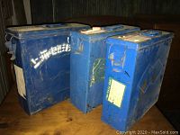 Three vintage blue metal film canister cases showing front and side views with various labels and wear.