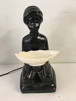 Front view of vintage ceramic black figurine lamp holding white ceramic bowl shaped light fixture.