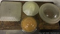 Four vintage glass light shades laid on a wooden surface showing different shapes and textures.