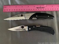 Two Spyderco folding pocket knives displayed with pink ruler for scale, showing one serrated blade measuring about 4 inches and one plain blade about 3.5 inches.
