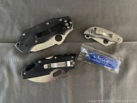 Four pocket knives arranged on gray surface showing the range of sizes and clips on handles.
