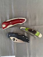 Three closed folding pocket knives with different handle materials and colors