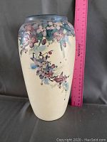 Front side of the cream ceramic vase with hand-painted flowers and pink ruler showing height about 9 inches.