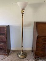Full view of vintage Art Deco metal floor lamp standing on carpeted floor, showing brass metal base, shaft, and milk glass shade on top.