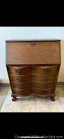Front view of the antique walnut secretary desk showing the curved front, drop-down lid closed, and four drawers with claw foot legs.