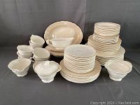 Full set arrangement showing stacks of various plate sizes, bowls, cups, saucers, and serving pieces in off-white floral embossed china.