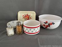 View of entire lot showing metal tray with floral motif, salt and pepper shakers, two small decorative bowls, and one Pyrex bowl with cherry decoration.
