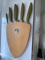 Five knives in wooden wall-mounted knife block with olive green handles on white background