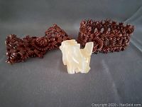 2 brown vintage Appleseed bracelets with carved wood pieces and a small carved stone dog figurine adjacent on gray background.