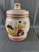 Front view of ceramic cookie jar with folk dancer figures and red stripe detailing.