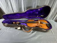 Violin and bow seated in open hard case showing purple velvet interior