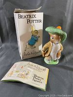 Figurine with original box and a small booklet laid out on black cloth background.