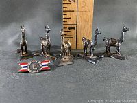 Photo showing set of six diecast llama figurines approximately 1 inch tall and a small enamel emblem with letter 'F'