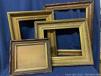 Four vintage picture frames against a dark blue backdrop, showing two gold gilded frames, one dark brown wood frame, one medium brown wood frame.