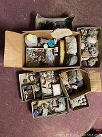 Overview photo showing multiple cardboard boxes filled with old rocks and mineral specimens of various sizes, colors and shapes.