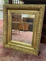 Full view of the vintage rectangular gilded mirror with floral patterned frame on the floor showing overall condition and style.