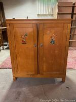 Front view of the vintage wooden pie cabinet showing two doors decorated with painted cartoon-like animal figures and silver round knobs. Scratches visible on surface.