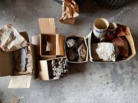 Top-down view of multiple cardboard boxes containing rocks, shale, and petrified wood pieces on a concrete floor.