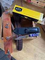 Photo showing boxed Buck knife, leather sheath, and two vintage brown leather belts on a table.