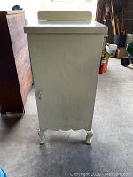 Side view of the white antique pie cabinet, showing its scalloped legs and flat top with raised back edge.