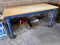 Full view of an old rectangular kitchen table with a natural maple wood top and blue painted turned legs showing wear and paint chipping.