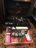 Overview of cases containing flatware and cutting tools in original lined cases on carpet