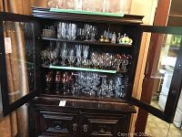 Front view of open upper glass doors displaying glassware and decorative items inside hutch.