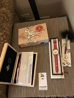 Wide view of wooden presentation box, red strap watch and pen on tabletop