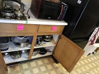 Two shelves inside a cabinet containing stainless steel pots, pans, plastic containers with lids, and kitchen appliances like waffle iron and bagel toaster.