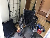 Invacare wheelchair with black armrests and blue padded seat on a carpet near door with metal grid shopping cart and box of supplies nearby.