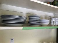 Shelf with stacks of dinner plates, dessert plates, and bowls in Somerset pattern by NL Excel.