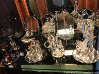 Full shelf of assorted Swarovski clear and colored crystal figurines displayed on mirrored surface inside wooden cabinet.